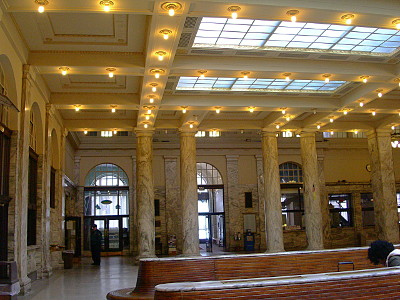 [Skylights add light to the buidling in addition to the many bulbs which are positioned across the beams of the roof. The columns are variegated marble and nearly two stories tall. The open space has wooden benchs with marble tops and heating vents positioned in the tops.]